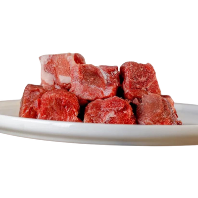 Sechs gefrorene Stücke von Hirschfleisch auf einem weißen Teller, unregelmäßige Form, rot und marmoriert.