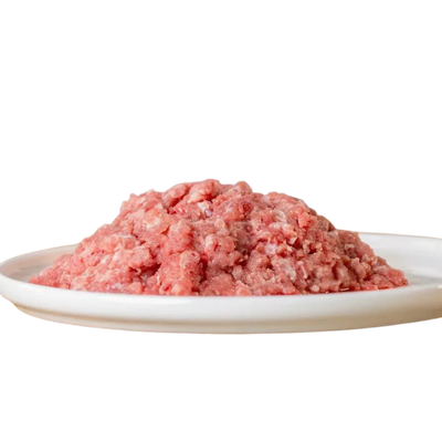 Haufen von gewolftem Hühnerhals auf einem weißen Teller. Produkt von Barfgold, 500g, für Tiere.