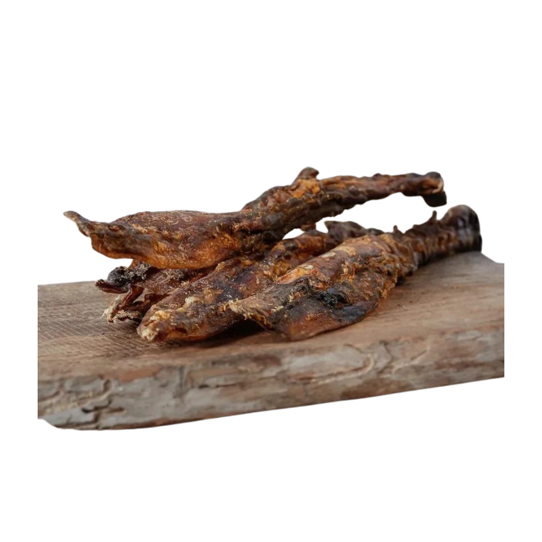 Drei getrocknete Hirschsehnen auf einem Holzbrett. Die Stücke sind länglich und unregelmäßig geformt, mit einer rauen Oberfläche.