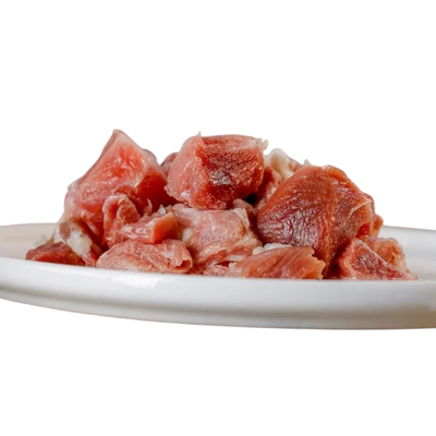 Rohes Putenfleisch in Würfeln auf einem weißen Teller. Die Stücke sind rot und rosa, variieren in der Größe.