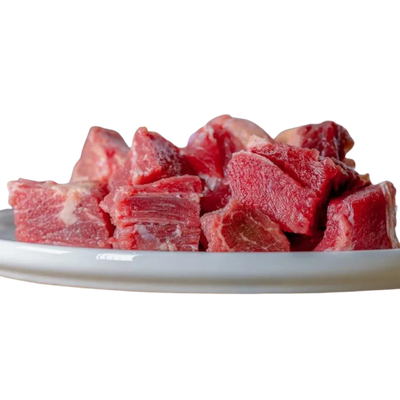 Auf einem weißen Teller liegen grob geschnittene Stücke durchwachsenes Rindfleisch, mit roten Muskelfasern und helleren Fettanteilen, roh und naturbelassen.