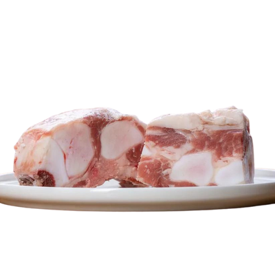 Zwei Stücke Kalbsbrustbein auf einem Teller. Das Fleisch hat eine marmorierte Struktur mit sichtbaren Knochen. Marke: Barfgold, Inhalt 1kg