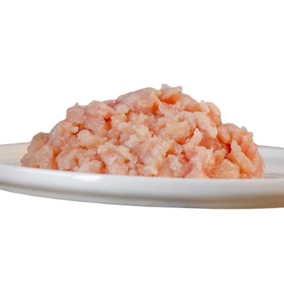 Haufen von gewolftem Hühnerfleisch auf einem weißen Teller. Die Textur ist fein und leicht rosa von der Marke Barfgold.