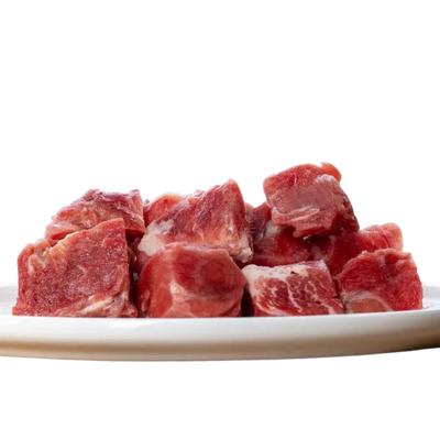 Weißer Teller mit Fleischstücken von der Ziege. Geformt in Würfel, einige mit und ohne Fett. Marke Barfgold