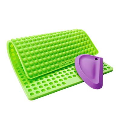 Grüne Silikonmatte mit Noppen und einer lila Kante, die eine abgerundete Form hat. Die Matte hat eine wellenförmige Struktur.
