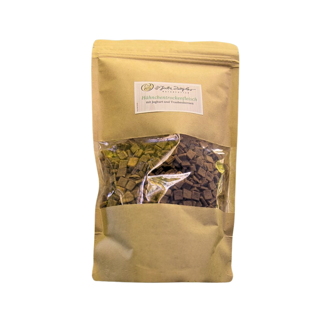 Beige Verpackung mit transparentem Fenster, gefüllt mit kleinen, dunklen Stückchen. Auf dem Etikett steht 'Hähnchentrockenenfleisch'.