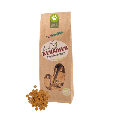 Papiertüte mit der Aufschrift 'Keksdieb Hundeleckerli Hüttenkäse', gefüllt mit quadratförmigen Hundekeksen, die vor der Tüte liegen.