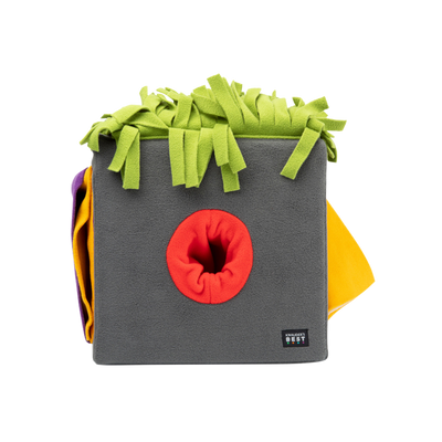 Graue Futterbox mit bunten, fransigen Stoffstreifen in Grün, Orange und Gelb. Die Box hat eine runde Öffnung in der Mitte.