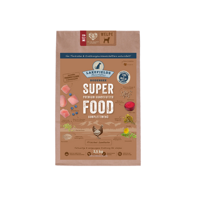 Verpackung von Lakefields Superfood für Hunde, 1 kg. Braune Tüte mit Bildern von Landhuhn, Kräutern und dem Text 'NEU' und 'WELPE'.