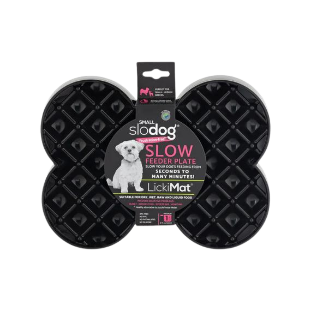 Schwarze Futterplatte 'LickiMat Slodog' in Form eines Knochens mit rautenförmigen Vertiefungen. Verpackung zeigt einen Hund und Informationen zur Verwendung.