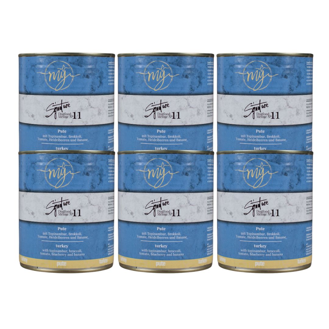 Sechs Dosen Hundefutter mit blauem Etikett. Aufschrift: my Signature, Dogfood Menue No. 11, BIO Pute und Zutaten wie Topinambur, Brokkoli, Heidelbeeren, Tomaten, Bananen,