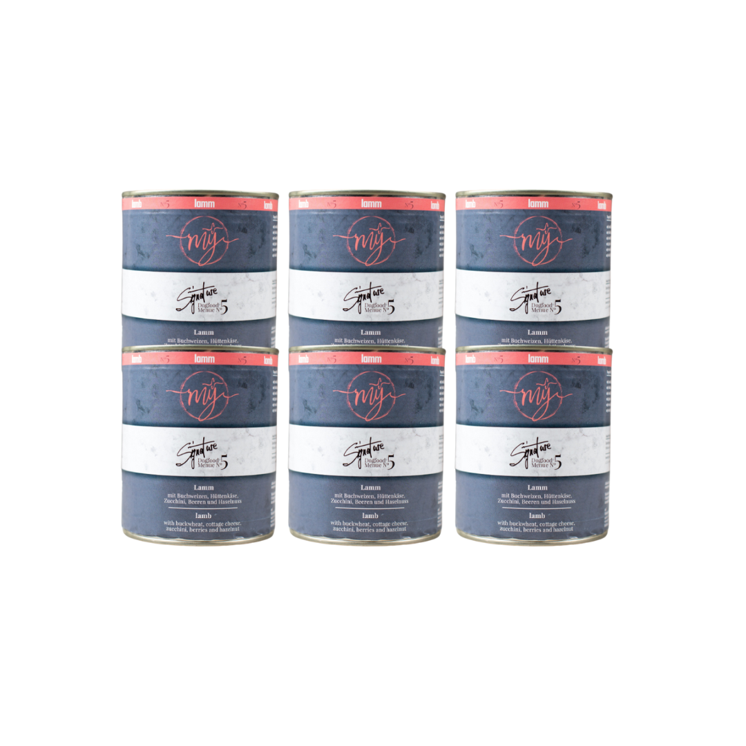 Sechs Dosen Hundefutter mit blauem Etikett. Aufschrift: my Signature, Dogfood Menue No.5, Lamm und Zutaten wie Buchweizen, Zucchini, Hüttenkäse, Cranberry, Heidelbeeren, Haselnuss