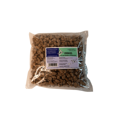 Transparente Verpackung mit 500 g Cookies von der Marke 'NEXT'. Die Cookies haben eine unregelmäßige Form und sind braun. Auf der Vorderseite befindet sich ein Etikett mit Produktinformationen.