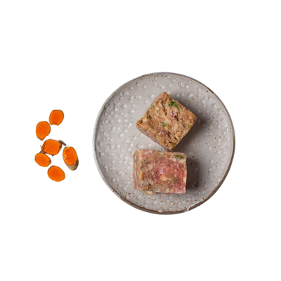 Zwei quadratische Stücke gemischtes Hackfleisch auf einem grauen, rundem Teller neben mehreren geschnittenen Karottenscheiben.