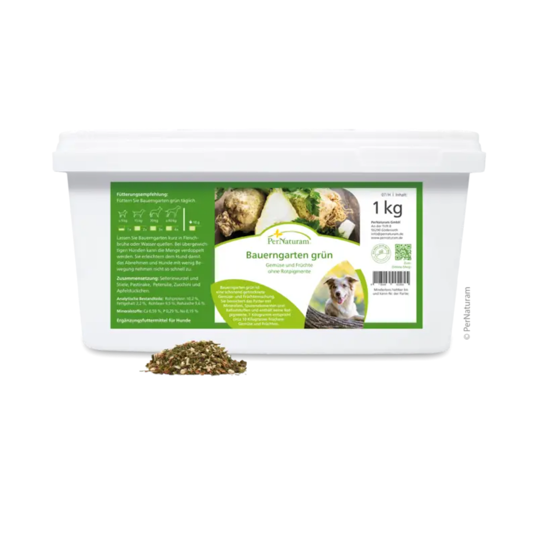 Weißer Behälter mit grünem Etikett der Marke PerNaturam, 1kg, Produktname 'Bauerngarten grün', mit Text "Gemüse und Früchte ohne Rotpigmente" und einem Bild eines braun und weißen Hundes, davor lose Kräutermischung.