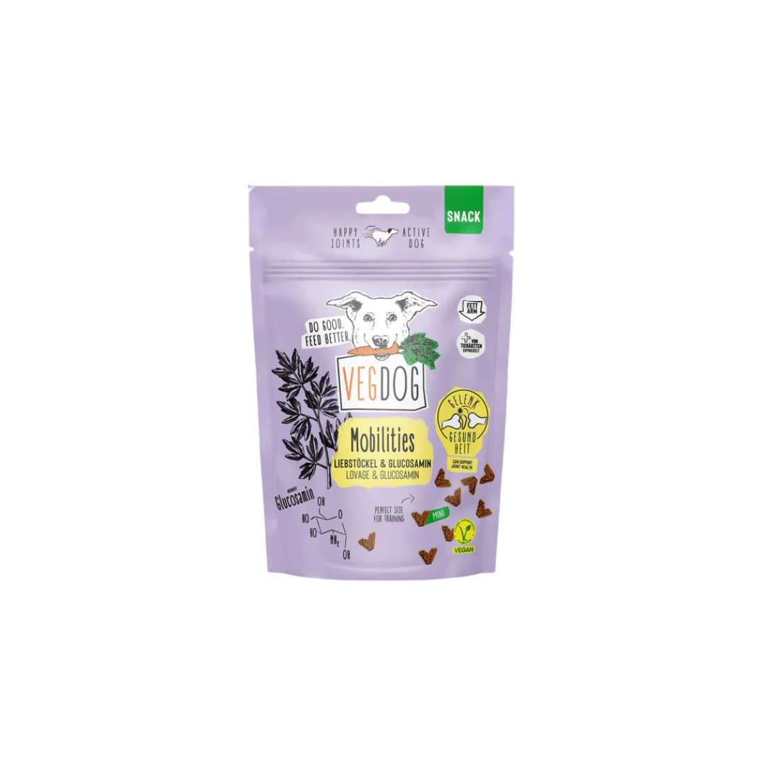 Lila Verpackung mit Hundekopf, Text 'VEGDOG Mobilities', kleine braune dreieckige Hundesnacks, Symbole für vegan und glutenfrei.