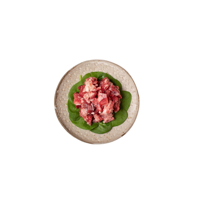 Würfel aus rohem Ziegenfleisch auf grünen Blättern auf einem runden Teller
