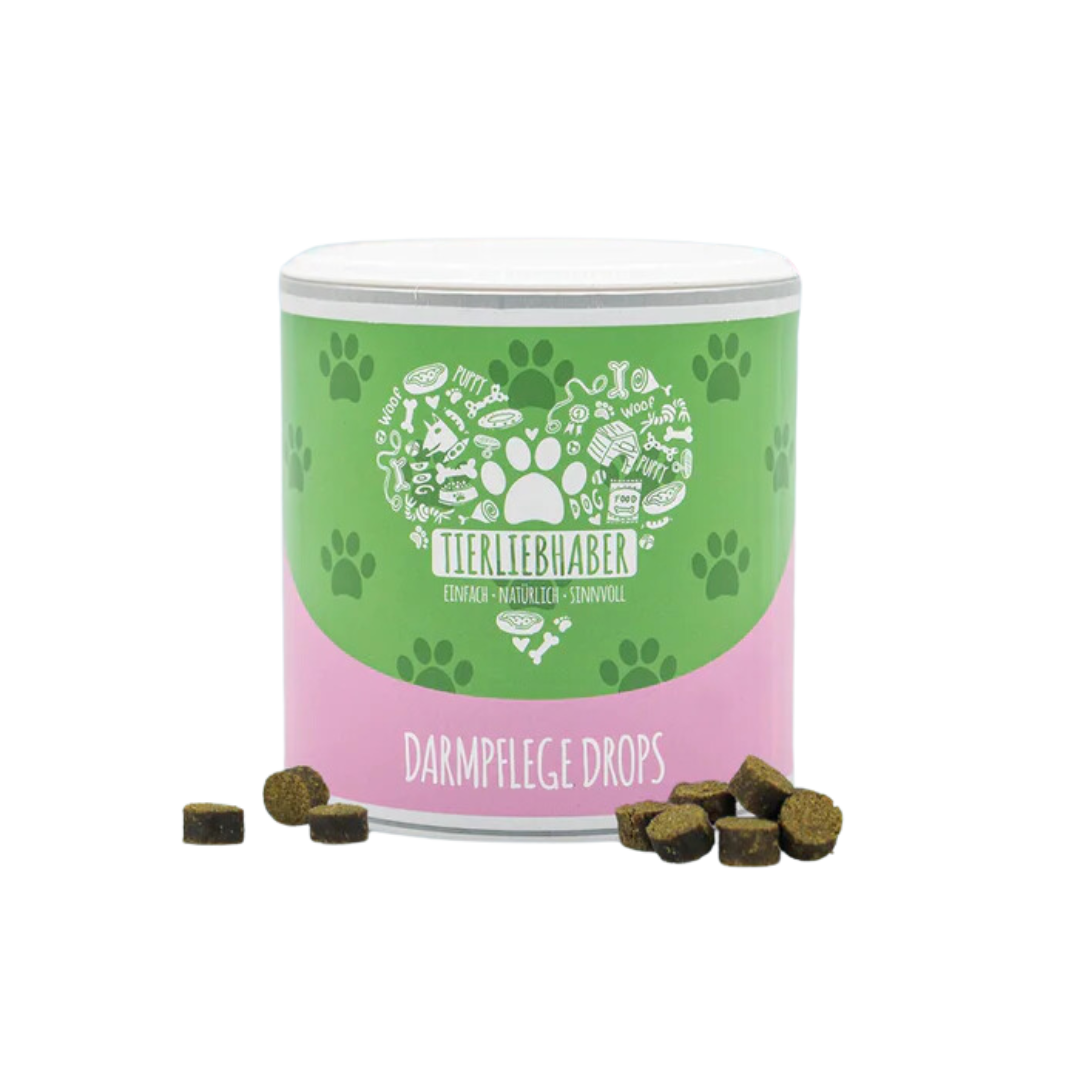 Grüne und rosa Dose mit der Aufschrift 'Tierliebhaber Darmpflege Drops', umgeben von kleinen braunen Drops, Pfotenmuster auf der Dose