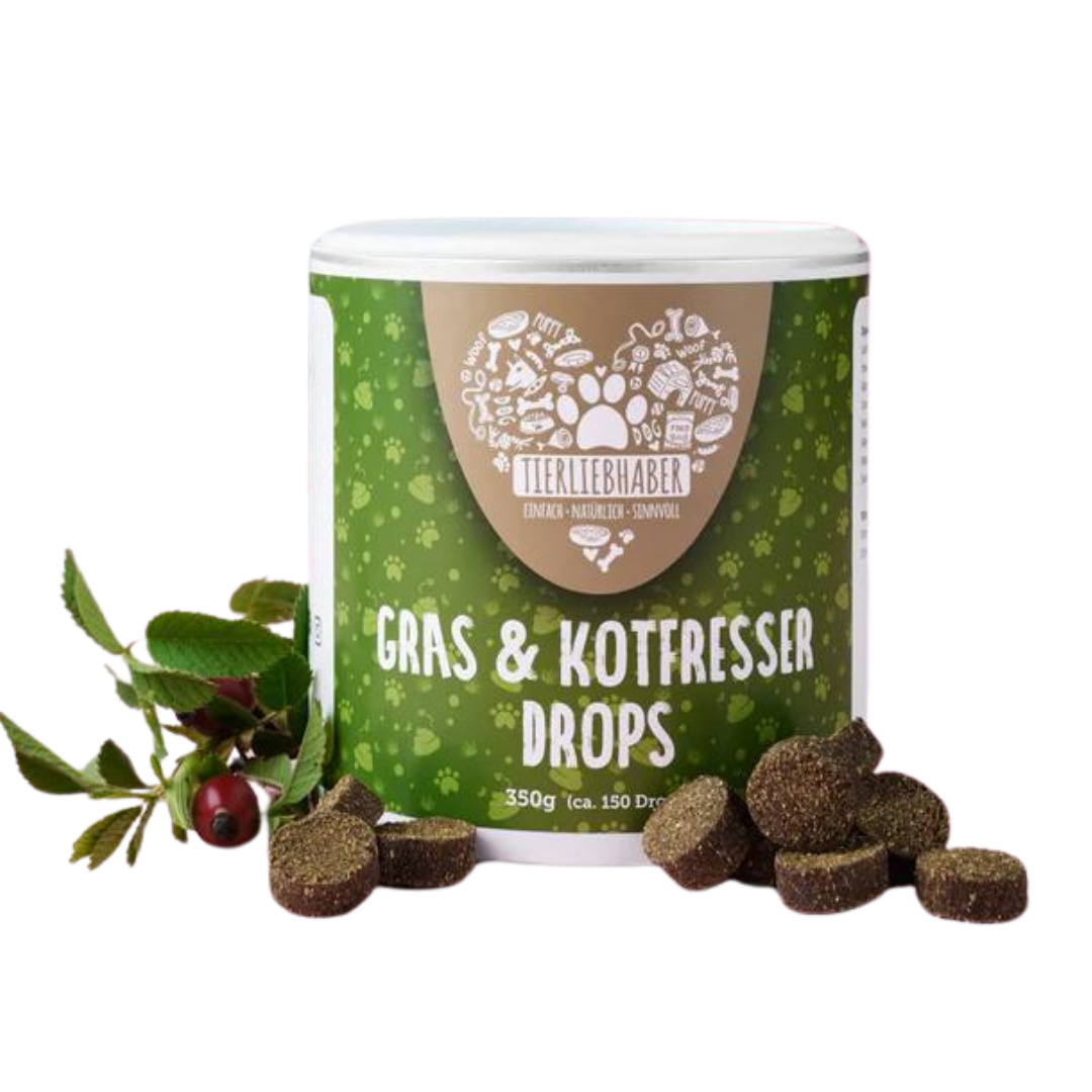 Weiß-grüne Dose mit der Aufschrift 'Tierliebhaber Gras & Kotfresser Drops 350g (ca. 150 Drops)' und braune runde Drops daneben, daneben Zweig mit roten Beeren.