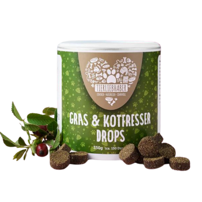 Weiß-grüne Dose mit der Aufschrift 'Tierliebhaber Gras & Kotfresser Drops 350g (ca. 150 Drops)' und braune runde Drops daneben, daneben Zweig mit roten Beeren.