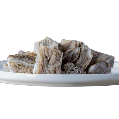 Stücke von getrocknetem Rindermagen auf einem weißen Teller. Die Stücke sind unregelmäßig geformt und zeigen eine schichtartige Struktur.