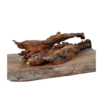 Drei getrocknete Hirschsehnen auf einem Holzbrett. Die Stücke sind länglich und unregelmäßig geformt, mit einer rauen Oberfläche.