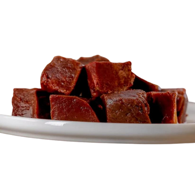 Stücke von Barfgold Pferdeherz auf einem weißen Teller. Die Stücke sind dunkelbraun und haben eine würfelförmige Form.