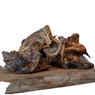 Getrocknete Pferdenackenknochen von Barfgold, in unregelmäßigen Formen auf einem Holzbrett angeordnet. Dunkelbraun mit rauer Oberfläche.