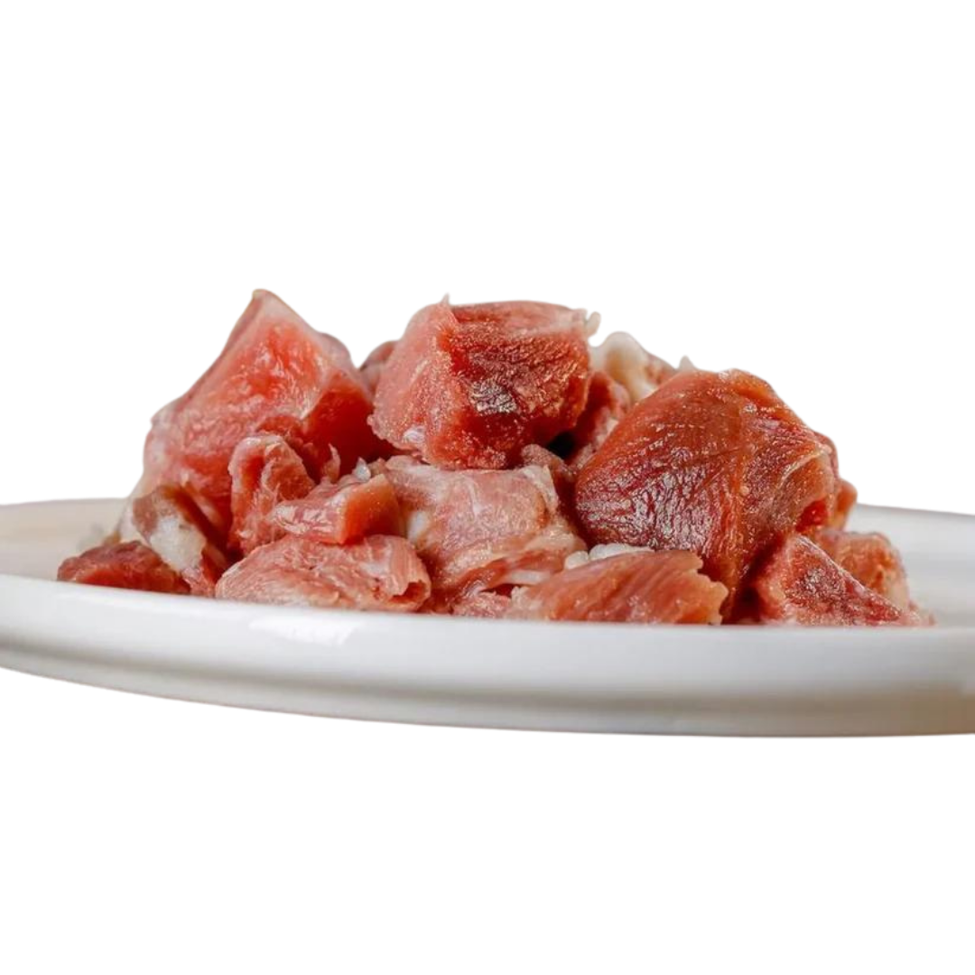 Rohes Putenfleisch in Würfeln auf einem weißen Teller. Die Stücke sind rot und rosa, variieren in der Größe.