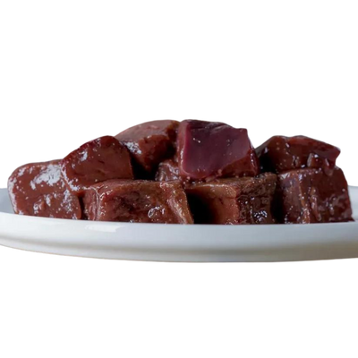 Stücke von Rindeleber auf einem weißen Teller, glänzende Oberfläche, in verschiedenen Größen und Formen, 500g. Marke: Barfgold.