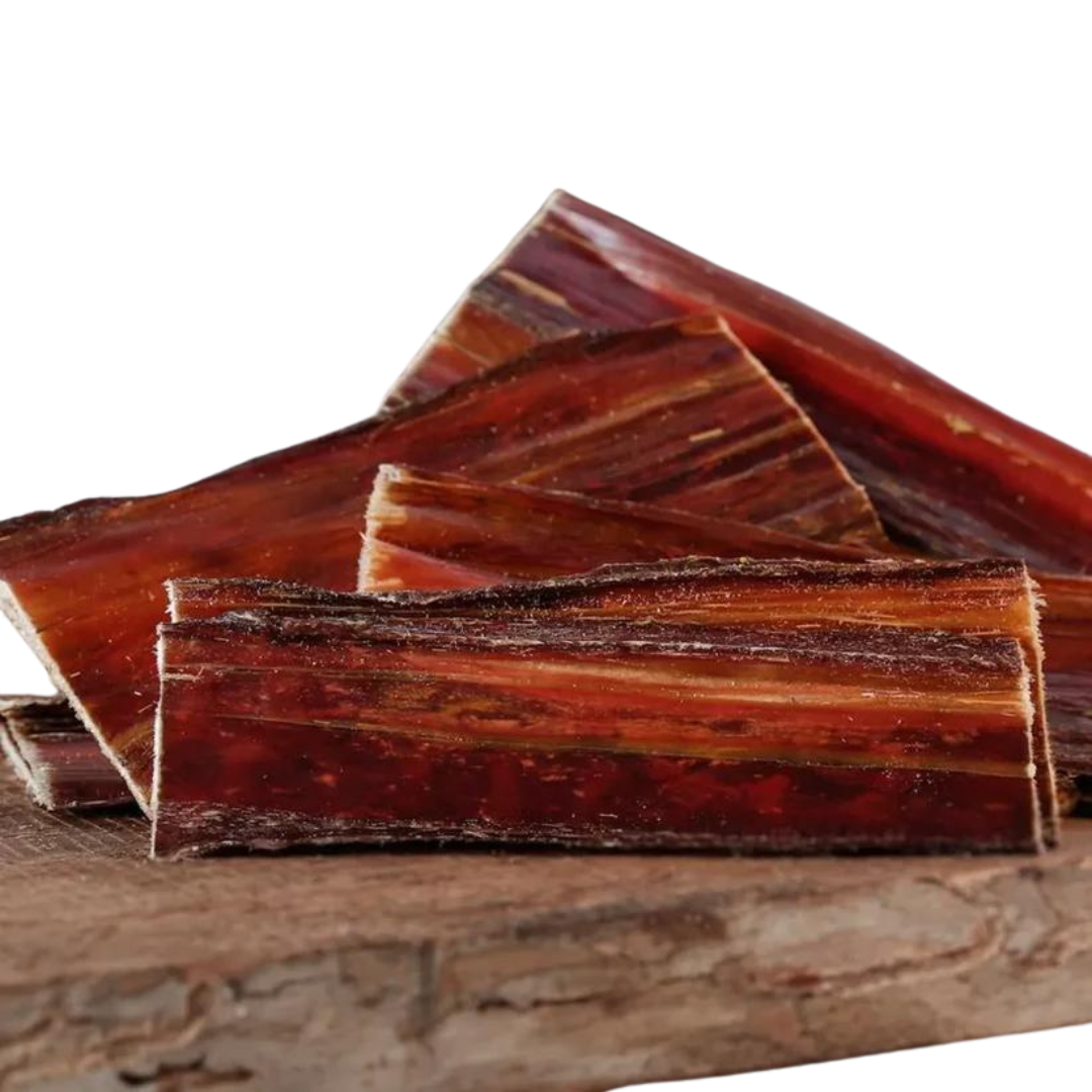 Stücke von Barfgold Rinderdorrfleisch, in verschiedenen Größen und Formen, auf einem Holzbrett angeordnet. Die Oberfläche zeigt eine schichtartige Struktur.