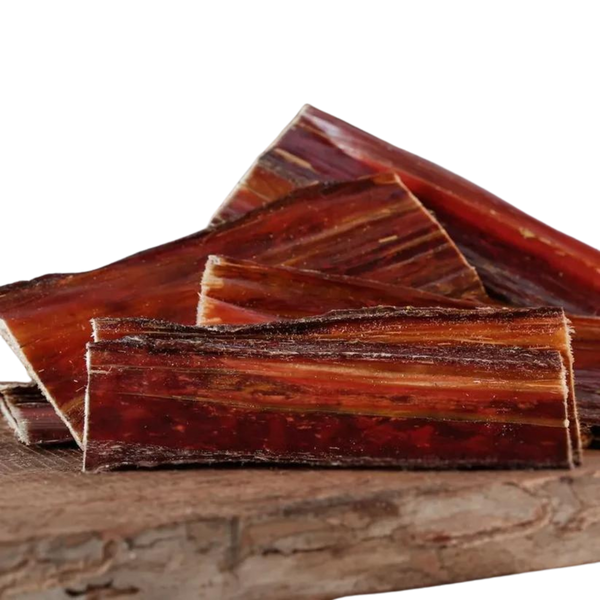 Stücke von Barfgold Rinderdorrfleisch, in verschiedenen Größen und Formen, auf einem Holzbrett angeordnet. Die Oberfläche zeigt eine schichtartige Struktur.