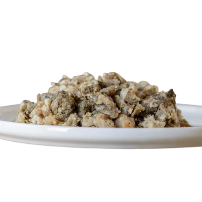 Auf einem weißen Teller liegt eine Portion gewolfter Rinderpansen, bestehend aus groben, unregelmäßigen Fleischstücken in verschiedenen Braun- und Grautönen.