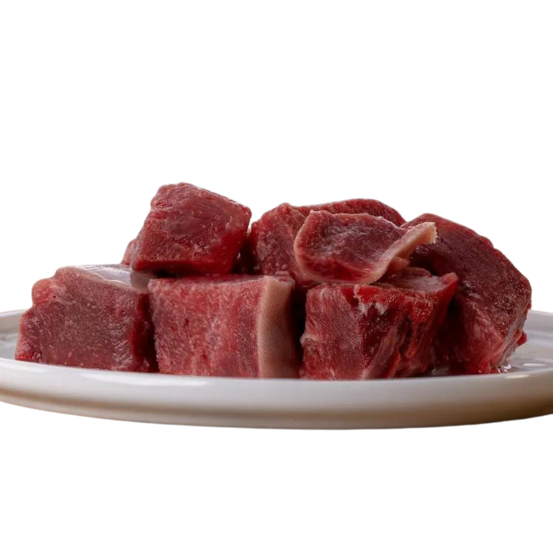 Auf einem weißen Teller liegen mehrere rohe Stücke magerer Rinderzunge in kräftigem Rotton, grob geschnitten und naturbelassen.