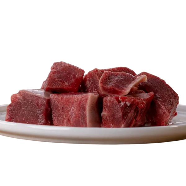 Auf einem weißen Teller liegen mehrere rohe Stücke magerer Rinderzunge in kräftigem Rotton, grob geschnitten und naturbelassen.