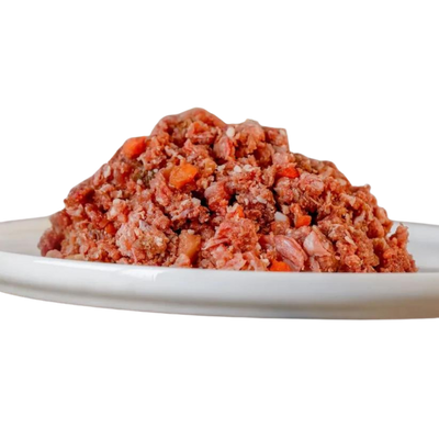 Barfgold Komplett Menü Lamm, 1 kg, auf einem weißen Teller. Das Futter ist grob gewolft und enthält sichtbare Stücke von Fleisch und Gemüse.