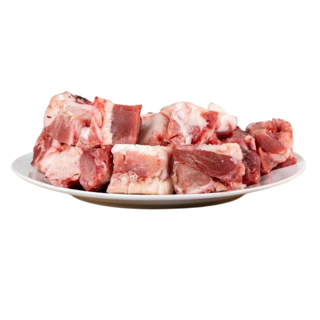Ein Teller mit Stückchen von Lammfleisch, einige mit Fett, in verschiedenen Formen und Größen. Produkt von Barfgold, 1 kg.