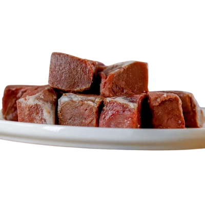 Sechs gefrorene, quadratische Stücke von Lammherz auf einem weißen Teller. Marke 'Barfgold'.