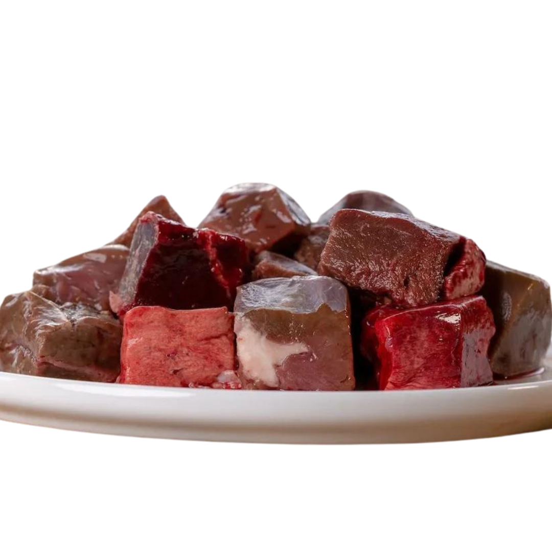 Stapel von gefrorenen Fleischwürfeln in verschiedenen Rottönen auf einem weißen Teller. Produkt: 'Barfgold TK Lamminnereienmix 1kg'.