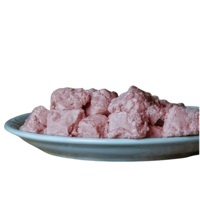 Barfgold Lammknochenmus in einer weißen Schüssel, bestehend aus rosa, würfelförmigen Stücken. Die Stücke sind unregelmäßig geformt und liegen übereinander.