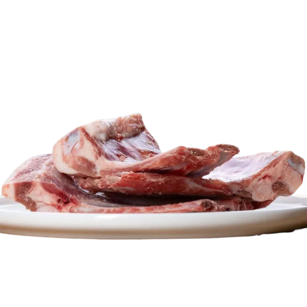 Rohes Lammrippchen auf einem weißen Teller, drei Stück sichtbar, mit sichtbarem Fleisch und Knochen.