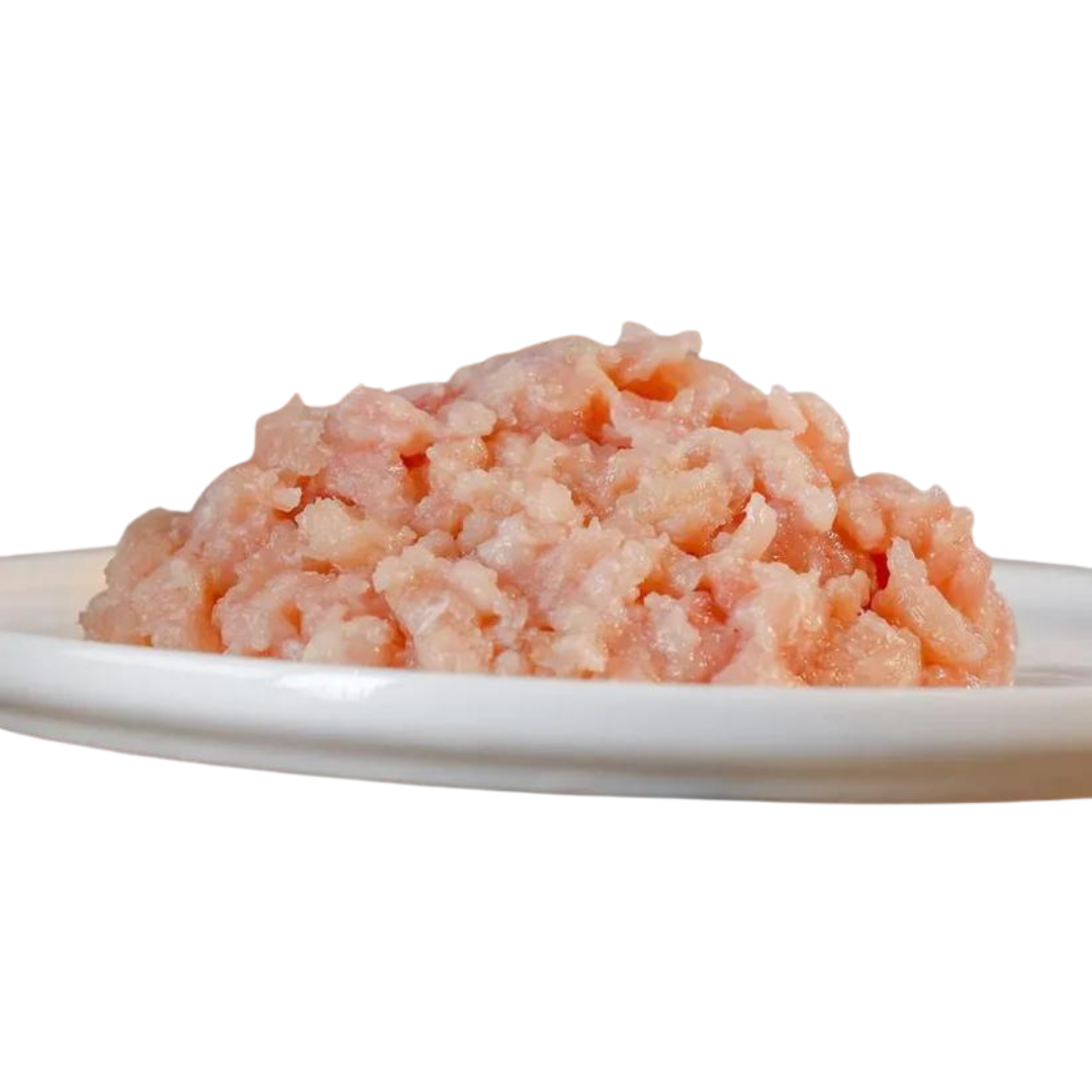 Haufen von gewolftem Hühnerfleisch auf einem weißen Teller. Die Textur ist fein und leicht rosa von der Marke Barfgold.