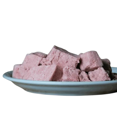 Eine weiße Schale mit einem Haufen rosa Würfeln, die Barfgold Pferdeknochenmus darstellen. Die Würfel sind unregelmäßig geformt und gestapelt.