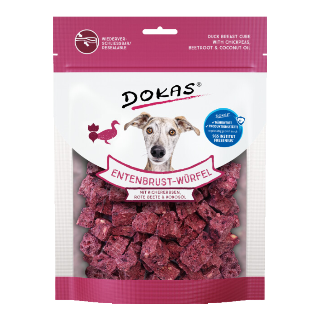 Verpackung von 'DOKAS Entenbrust-Würfel' mit einem Bild eines Hundes, der direkt in die Kamera schaut. Die Verpackung zeigt lila Würfel, die aus Entenbrust, Kichererbsen, roter Beete und Kokosöl bestehen.