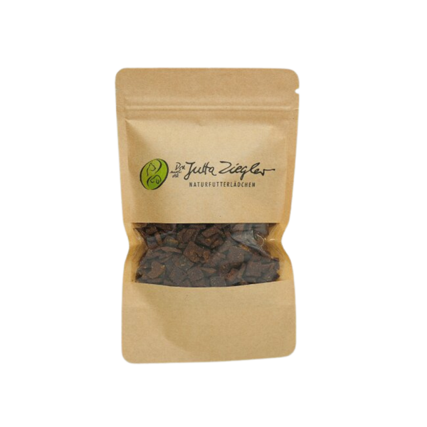 Braune Papiertüte mit transparentem Fenster, gefüllt mit kleinen, dunklen Snacks. Auf der Tüte steht 'Das ist Jutta Ziegler NATURFUTTERLÄDCHEN'.