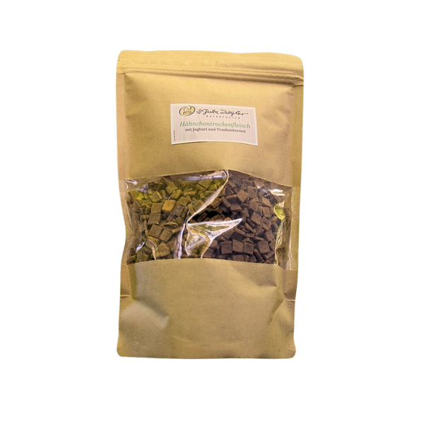 Beige Verpackung mit transparentem Fenster, gefüllt mit kleinen, dunklen Stückchen. Auf dem Etikett steht 'Hähnchentrockenenfleisch'.