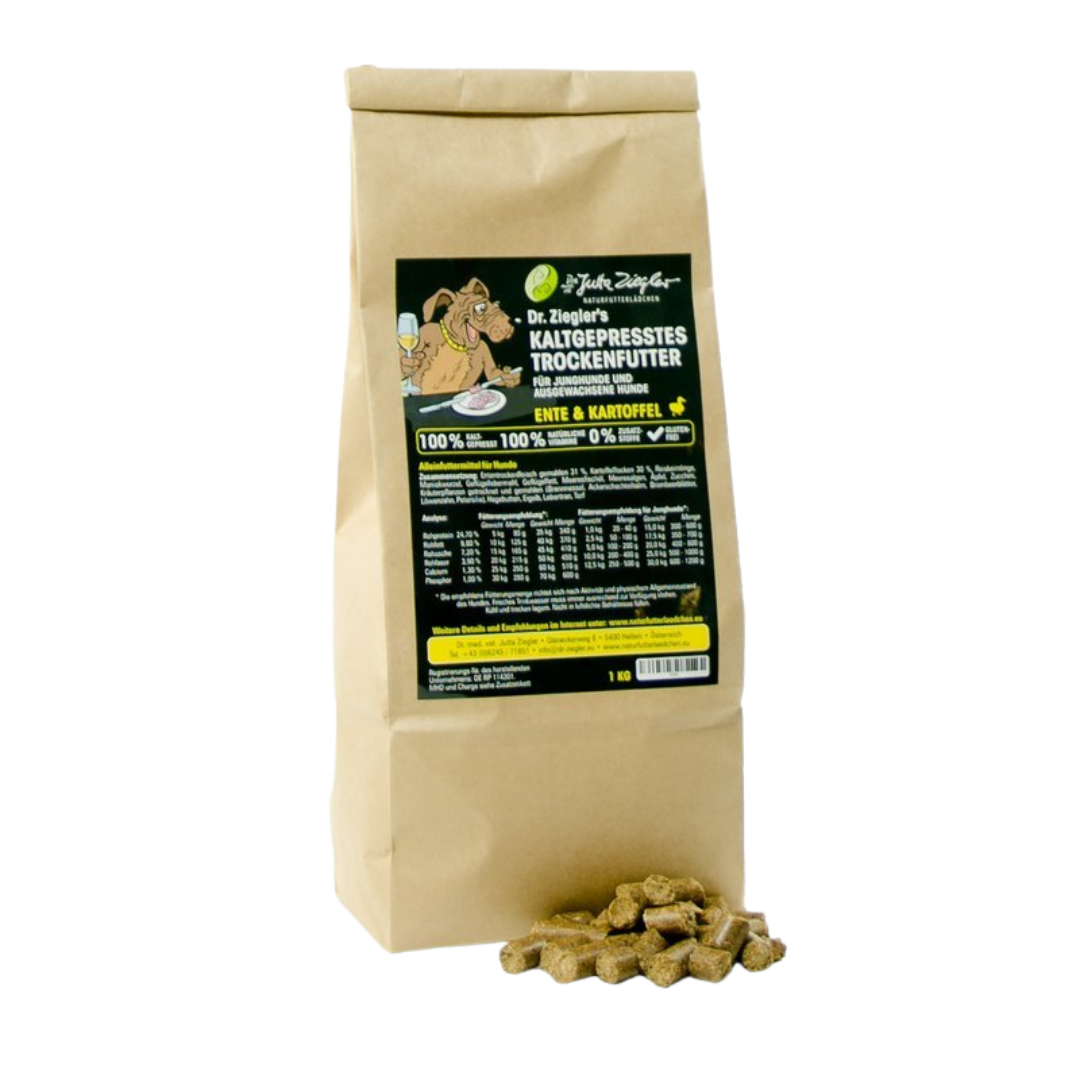 Braune Papiertüte mit schwarzem Etikett, beschriftet mit 'Dr. Ziegler's KALTGEPRÄSSTES TROCKENFUTTER', enthält Trockenfutter für Hunde mit Enten- und Kartoffelanteil. Vor der Tüte liegen einige Futterpellets.