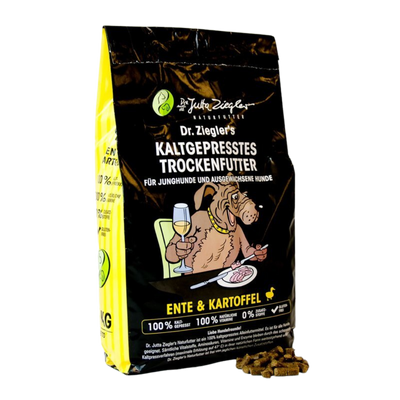 Schwarze Verpackung mit dem Text 'Dr. Ziegler's KALTGEPRRESSES TROCKENFUTTER FÜR JUNGHUNDE UND AUSGEWACHSENE HUNDE' und einem Hund, der ein Glas hält. Enthält Trockenfutter aus Ente und Kartoffeln.