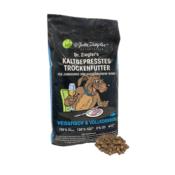 Schwarze Verpackung von Dr. Ziegler's kaltgepresstem Trockenfutter für Hunde mit Illustration eines Hundes, der an einem Tisch sitzt und Wein trinkt, Text 'Weissfisch & Vollkornreis' und Futterstückchen daneben.