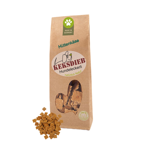 Papiertüte mit der Aufschrift 'Keksdieb Hundeleckerli Hüttenkäse', gefüllt mit quadratförmigen Hundekeksen, die vor der Tüte liegen.